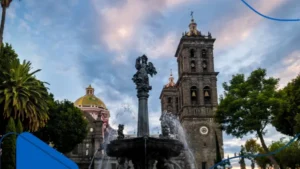 Fotografía panorámica en un atardecer de una fuente y catedral en Puebla: Una de las ciudades para comprar casa en México